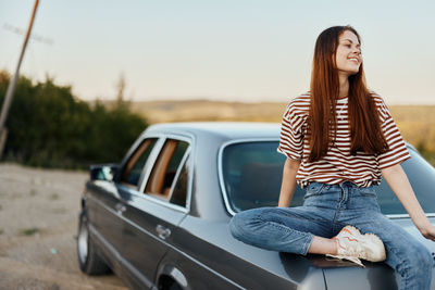 Portrait of young woman sitting on car