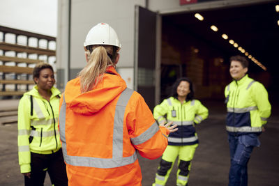 Rear view of female engineer in protective workwear discussing with workers at factory