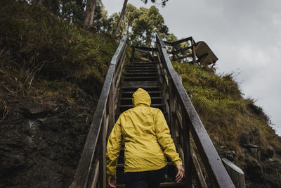 Rear view of woman in raincoat climbing staircase during rainy season