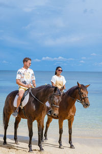 Man and woman riding horse on beach against sky