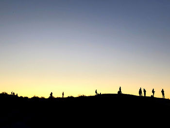 Silhouette people on field against clear sky during sunset