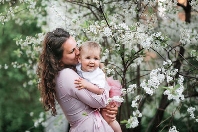 Portrait of smiling young woman standing by cherry blossom