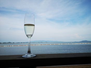 Glass of water on table by sea against sky