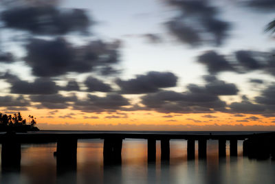 Silhouette bridge over sea against sky during sunset