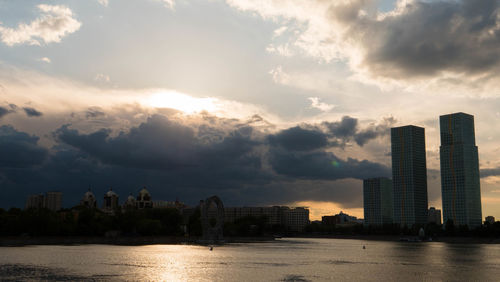 Sea by modern buildings against sky during sunset