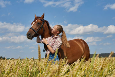 Smiling woman with horse standing at farm against sky