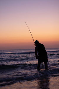 A man preparing his fishing rod in the shore at sunset.