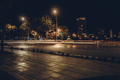 Illuminated street by buildings against sky at night