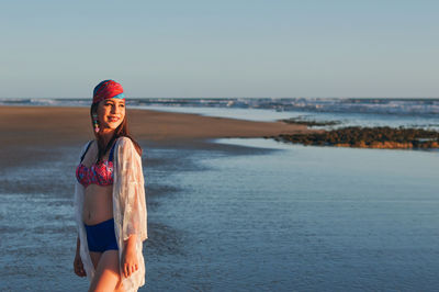 Young woman standing at beach against sky