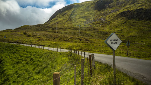 Road sign by agricultural landscape against sky