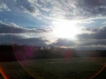 Sun shining through clouds over grassy field