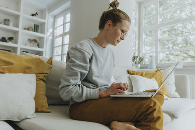 Mid adult woman working on laptop while sitting on sofa at home