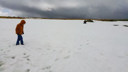 Full length of child walking on snow covered field against sky