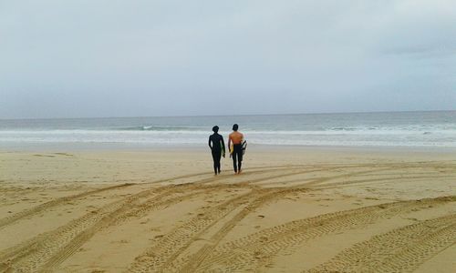 Rear view of friends walking on beach against sky