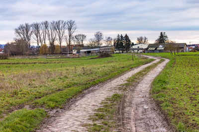 Scenic view of dirt road next to agricultural field against cloudy sky