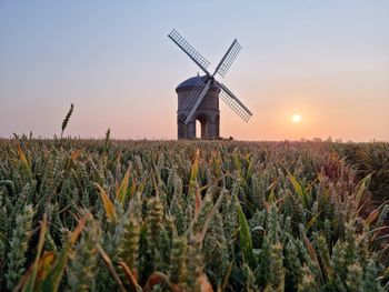 Traditional windmill on field against sky during sunset