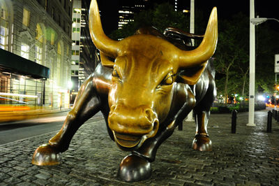 Statue against illuminated street and buildings at night