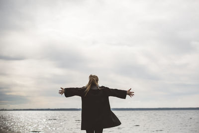 Rear view of woman standing by sea against sky