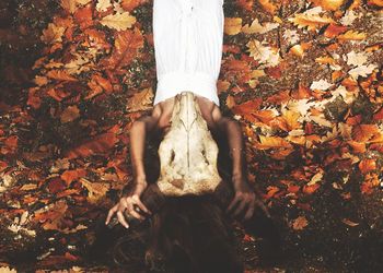 High angle view of woman holding skull while lying on fallen dry leaves