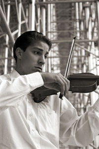 Man playing violin while standing against scaffolding