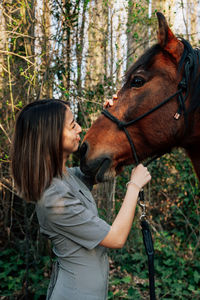 Smiling woman standing by horse against trees