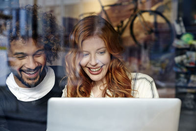 Happy young couple using laptop behind windowpane