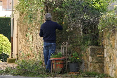 Rear view of man standing by plants in yard