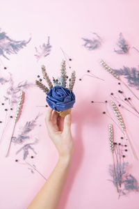 Cropped hand of woman holding decoration over pink background