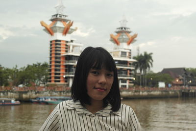 Portrait of young woman by river in city