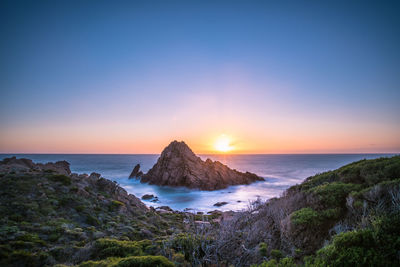 Scenic view of sea and cliff against sky during sunset