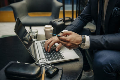 Midsection of businessman holding credit card using laptop at hotel lounge