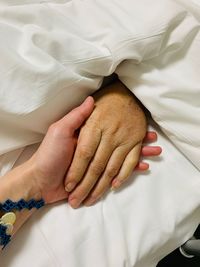 Cropped image of people holding hands on bed at hospital