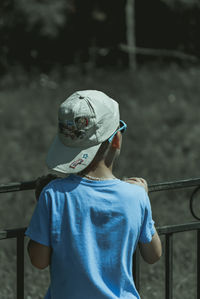 Rear view of boy wearing cap while leaning on railing