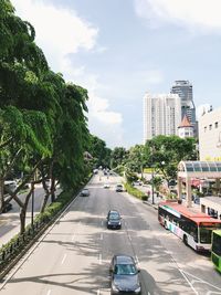 Cars on road by buildings in city against sky