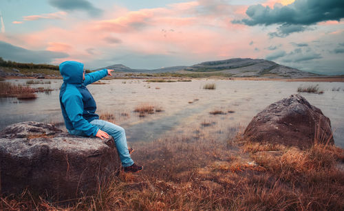 Hiker in sitting on the rock by the lake and watching sunset, mountain, burren , clare, ireland