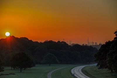 Road by trees against clear sky during sunset