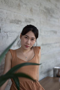 Portrait of young woman sitting against wall