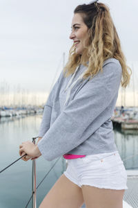 Beautiful smiling woman standing by railing on boat deck at harbor