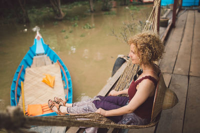 Side view of mid adult woman with hat sitting on hammock over lake