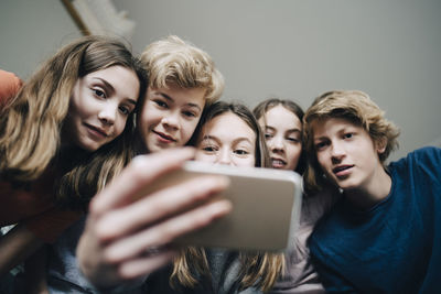 Low angle view of friends taking selfie through smart phone at home