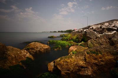 Rocks on shore by sea against sky