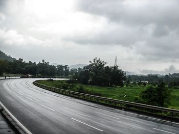 Road leading towards mountains against cloudy sky