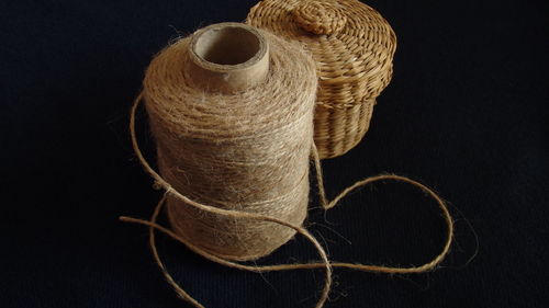 Close-up of spool by wicker basket over black background
