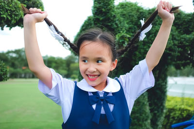 Smiling girl looking away while holding braided hair at park