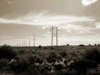 Electricity pylon on field against cloudy sky