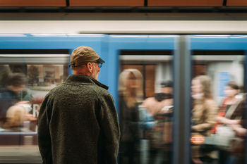 REAR VIEW OF MAN STANDING AT RAILROAD STATION PLATFORM