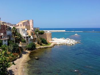 Scenic view of sea by buildings against clear blue sky