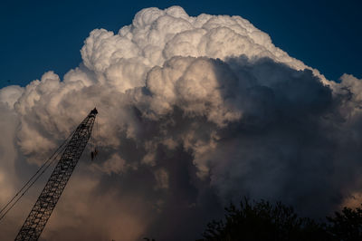 Low angle view of crane against sky and clouds