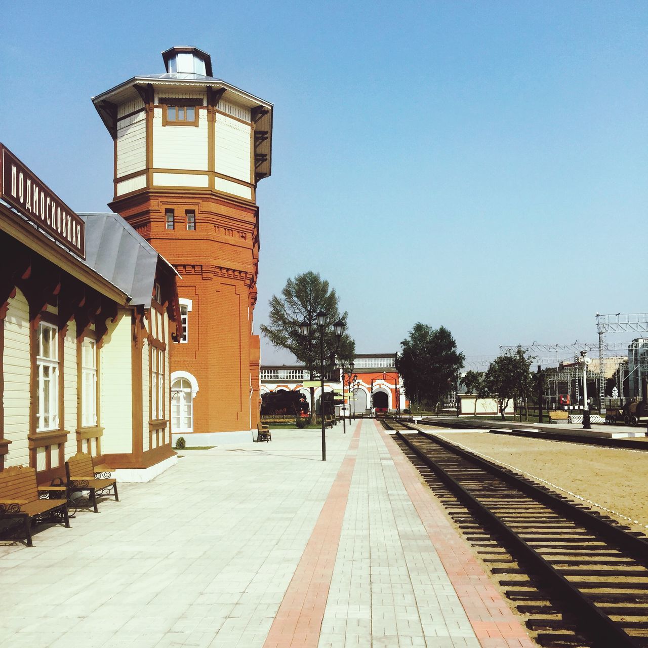 building exterior, architecture, built structure, clear sky, the way forward, transportation, street, street light, city, incidental people, road, tree, outdoors, copy space, blue, sky, day, footpath, building, sunlight