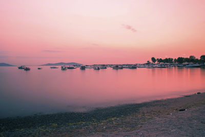 Boats moored in sea against pink sky during sunset